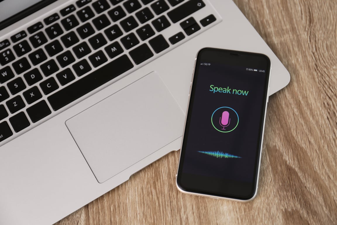 Smartphone with Activated Voice Search App and Laptop on Wooden